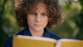 Close-up portrait of concentrated boy reading book outdoors on sunny day. Headshot of intelligent Caucasian kid studying enjoying literature. Slow motion - Powered by Shutterstock - Get 15% off with code: PIKWIZARD15