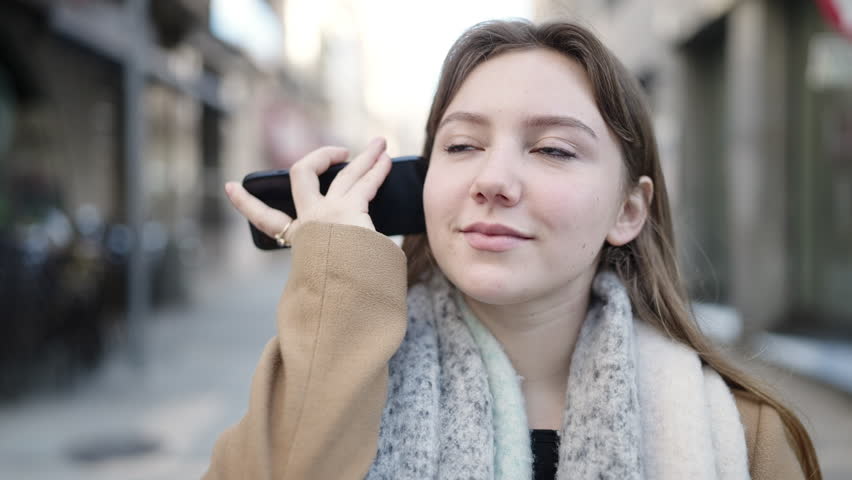 Young blonde woman smiling confident listening audio message by the smartphone at street | Shutterstock HD Video #1101850733