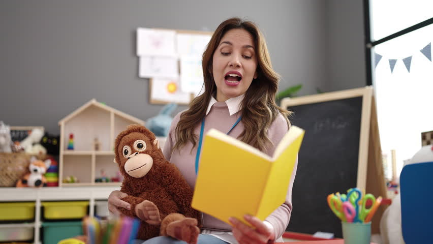 Young beautiful hispanic woman preschool teacher reading story book at kindergarten | Shutterstock HD Video #1101851039