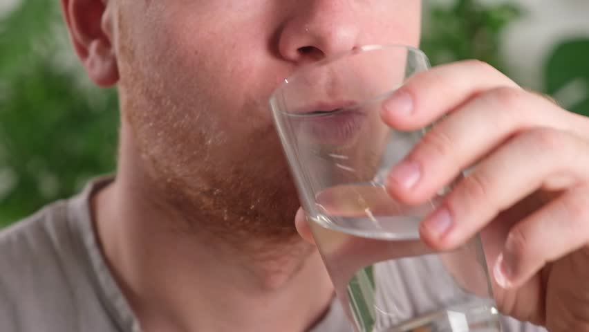 Caucasian man taking a pill and drinking a glass of water. Young man taking vitamin indoors. Health, medicine, treatment concept.
