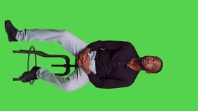 Vertical video: Front view of african american man on chair posing with confidence, sitting over full body green screen backdrop. Young male model feeling optimistic and waiting for something in - Powered by Shutterstock - Get 15% off with code: PIKWIZARD15