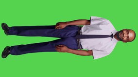 Vertical video: Side view of african american businessman posing in studio over full body greenscreen backdrop, feeling confident wearing formal business suit on camera. Male company employee feeling