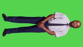 Vertical video: Front view of african american businessman posing in studio over full body greenscreen backdrop, feeling confident wearing formal business suit on camera. Male company employee feeling