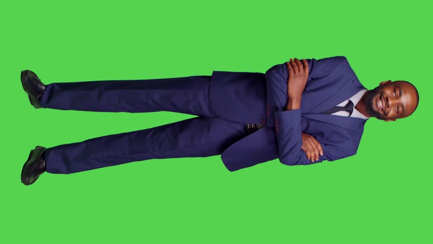 Vertical video: Front view of startup manager feeling confident on camera, wearing business suit to work on corporate job. Smiling adult entrepreneur posing over greenscreen full body background