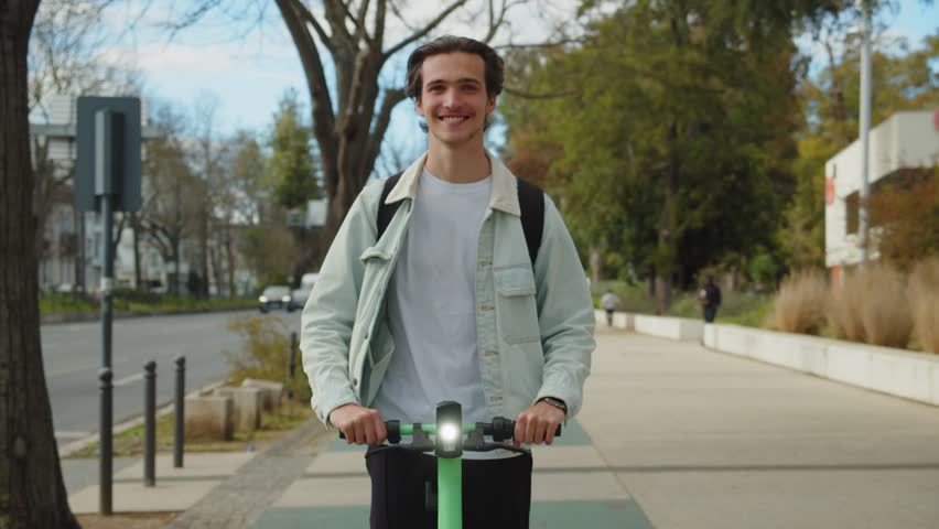 Young smiling man rides an electric scooter in the city on a sunny day. Happy student riding on a rented green electric scooter through the streets of the city. Ecological transport. Slow motion Royalty-Free Stock Footage #1101853645
