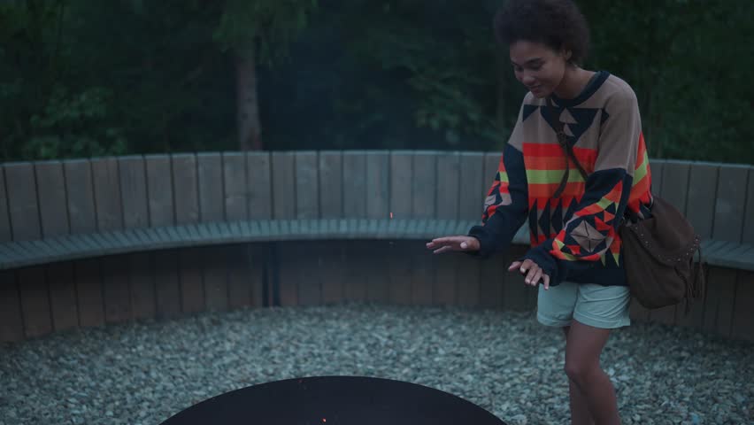 Handsome young African woman warming her hands by the fire in the mountains