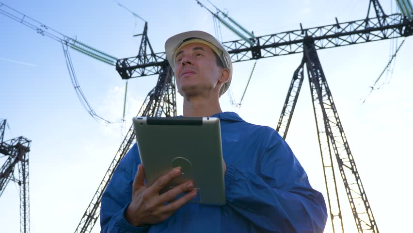 Power energy engineer stands electrical tower with tablet in his hands. Engineer will use tablet work with power energy lines. Technologies in electric power industry. Work engineer electrical towers. Royalty-Free Stock Footage #1101856715