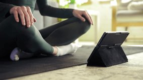 Yoga and meditation. Young girl in sportswear sitting on fitness matt and scrolling videos on tablet, choosing online training at home. Concept of sportive and healthy lifestyle, wellness, care.