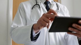 Close up of a doctor using a tablet computer in a hospital. The unrecognizable man is standing outside a doctor's office wearing white coat and stethoscope. - Powered by Shutterstock - Get 15% off with code: PIKWIZARD15