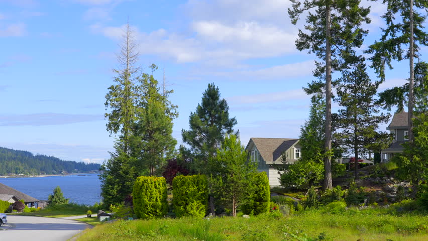 Establishing shot of two story stucco luxury house with garage door, big tree and nice spring blossom landscape in Vancouver, Canada, North America. Day time on May 2022. ProRes 422 HQ.