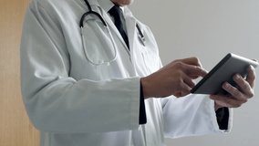 A doctor using a tablet computer in a hospital. The unrecognizable man is standing outside a doctor's office wearing white coat and stethoscope. - Powered by Shutterstock - Get 15% off with code: PIKWIZARD15