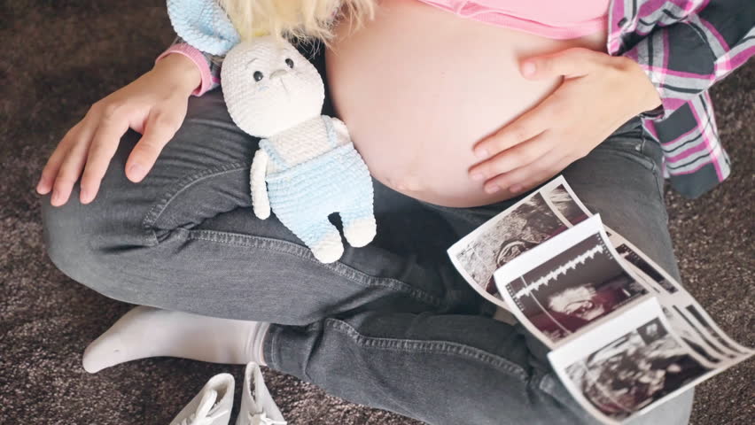 Ultrasound scan pictures to reveal baby gender, happy mother sitting on the floor and stroking gently her pregnant belly, medical examination before childbirth, maternity concept
