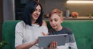 Happy millennial caucasian mom with her son use tablet device, playing video game on tablet computer, using online app, service, chatting