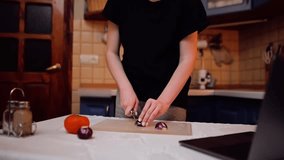 A girl is cutting vegetables and communicating with someone via a web-cam or viewing content using a laptop
