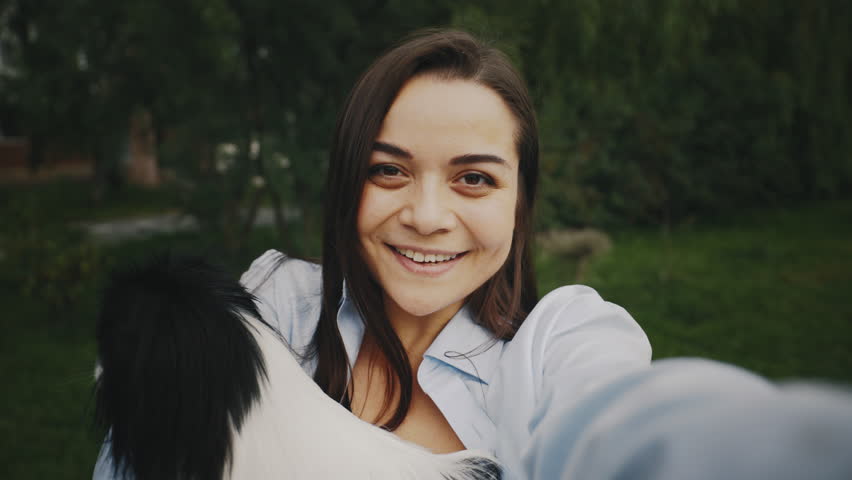 POV of Happy Beautiful Caucasian Woman Holding Her Japanese Chin Dog and Making Video Call, Chatting with Friends. Attractive Girl Recording Video for Blog. Female Talks on Webcam Standing Outside | Shutterstock HD Video #1101867485