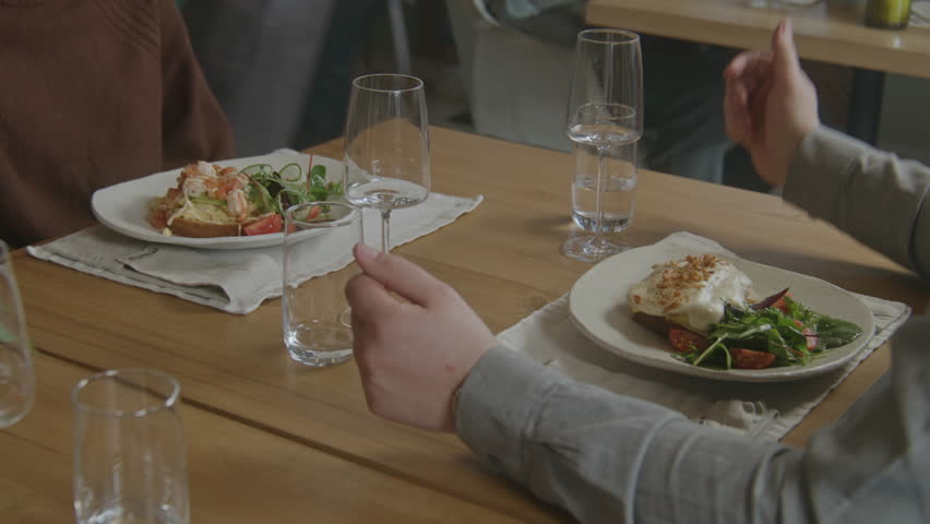 Male waiter in uniform brings plates with gourmet dishes to guests. Group of friends celebrate birthday in cafe with modern cuisine. Wine glasses and flowers stands on table. Concept of public eating. | Shutterstock HD Video #1101868929