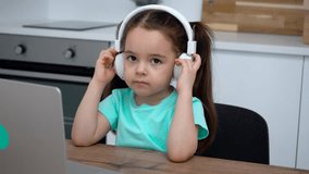 Little girl with headphones and glasses studies online communicates with a tutor
