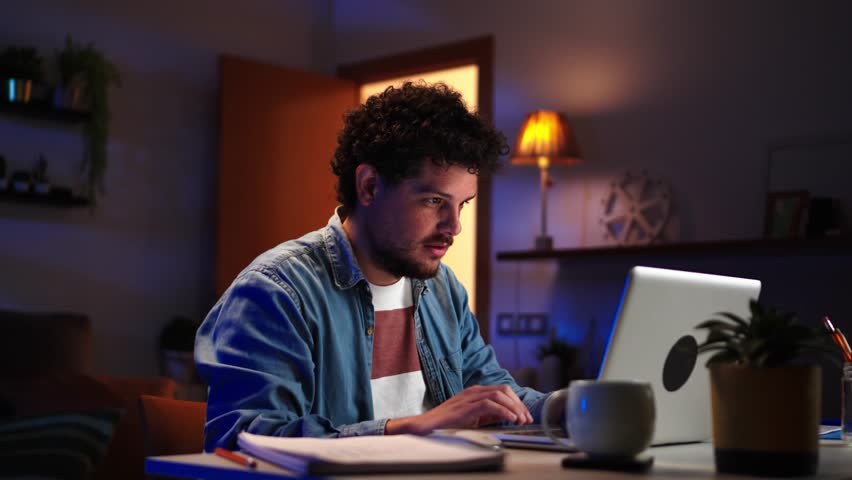 Seirous young caucasian freelancer man working at home with laptop computer writing with pencil in a notepad. Entrepreneur professional male checking finances on internet sitting at desk at night Royalty-Free Stock Footage #1101872797