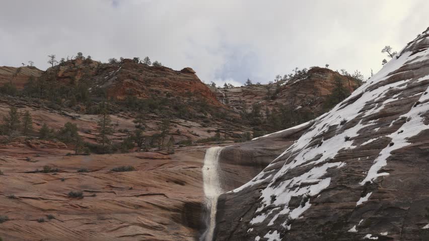 Ephemeral waterfalls pour down the red sandstone cliffs into Clear Creek in Zion Nat. park, Utah, USA, as storm clouds break up and drift through the sky overhead.