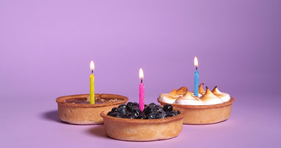 Different tartlets with burning festive candles on violet background