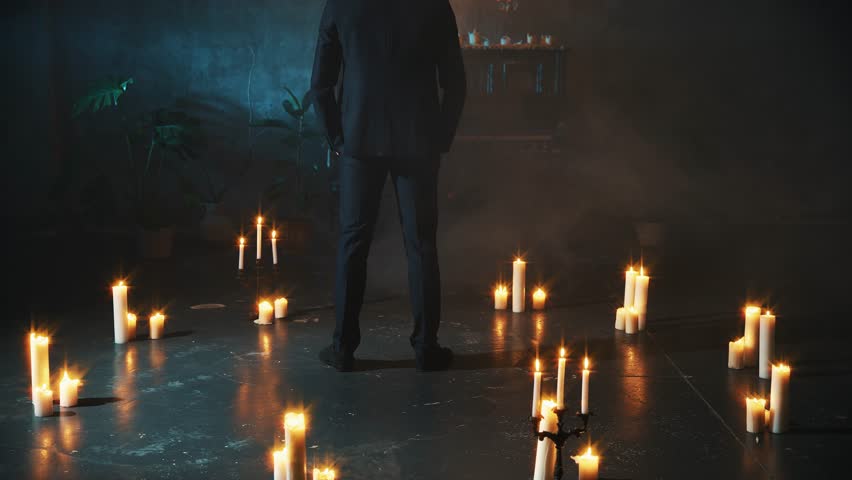 sexy couple blonde woman back rear view approaches man seduces strokes with hand. Gothic Girl touching guy. Portrait Fashion model Black suit. dark room fantasy carnival ball scenery candles burning