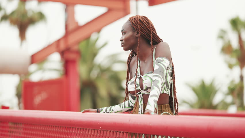 Gorgeous woman with braids wearing top stands on the bridge