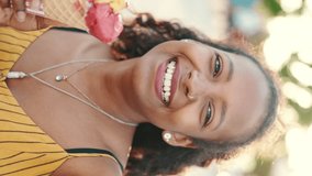 VERTICAL VIDEO, Closeup of smiling young woman with long curly hair on an urban city background with ice cream in her hands. Frontal close-up of happy girl testing ice cream on warm sunny day