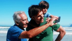 Abstract shapes over vibes text against grandfather, father and son having a video call at beach. travel and vacation concept