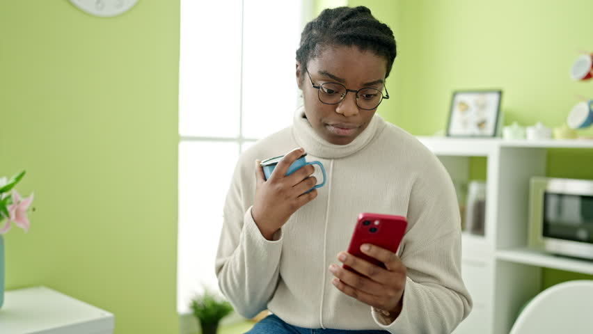 African american woman using smartphone drinking coffee at dinning room