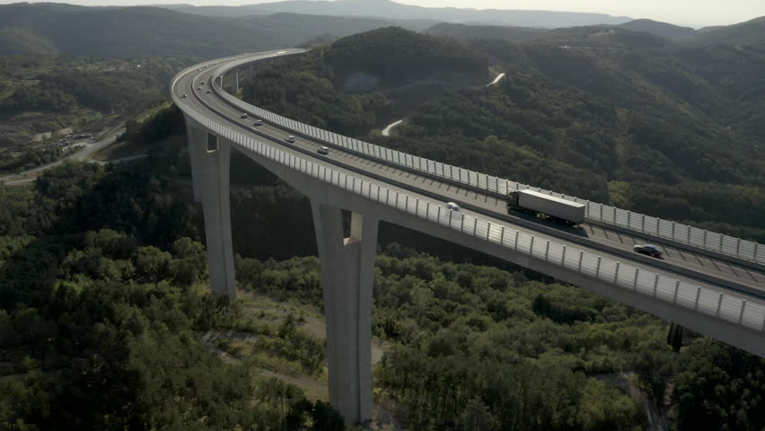 Aerial - Distant tracking shot of all white cargo truck driving on a highway through a bridge Royalty-Free Stock Footage #1101895529