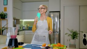 Senior woman in casual home clothes prepares healthy cocktails with different seasonal fruits.