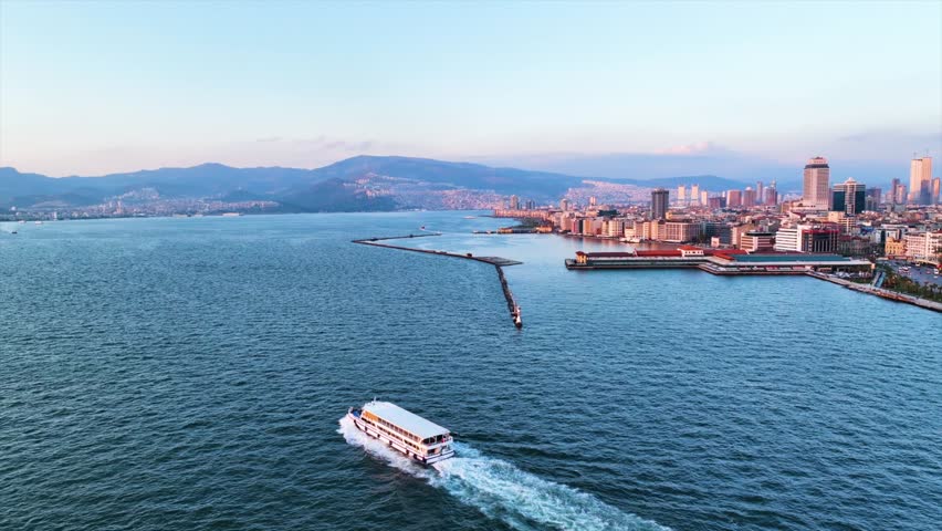 Aerial tracking of the steamboat advancing in the Aegean Sea with the view of Izmir at sunset. Royalty-Free Stock Footage #1101896297