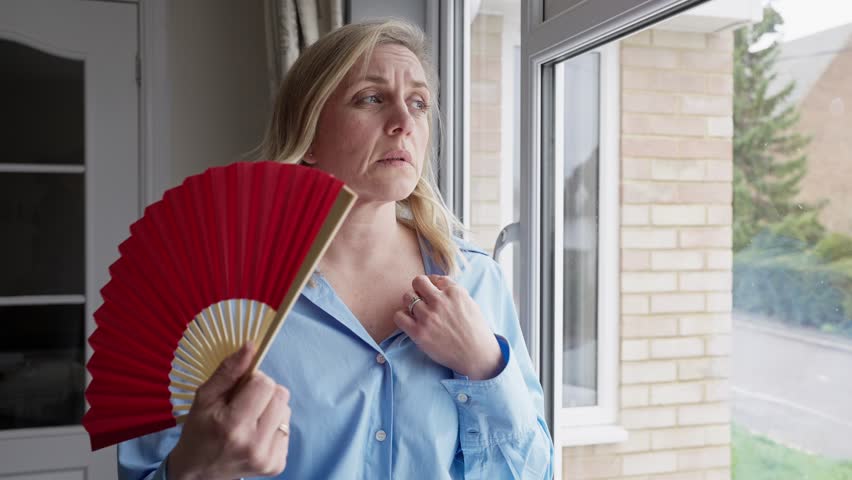 Menopausal Mature Woman Having Hot Flush At Home Cooling Herself With Handheld Paper Fan  Royalty-Free Stock Footage #1101896373