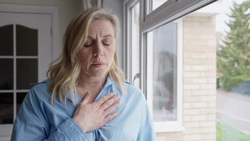 Menopausal Mature Woman At Home Standing By Window Suffering With Heart Palpitations Royalty-Free Stock Footage #1101896413