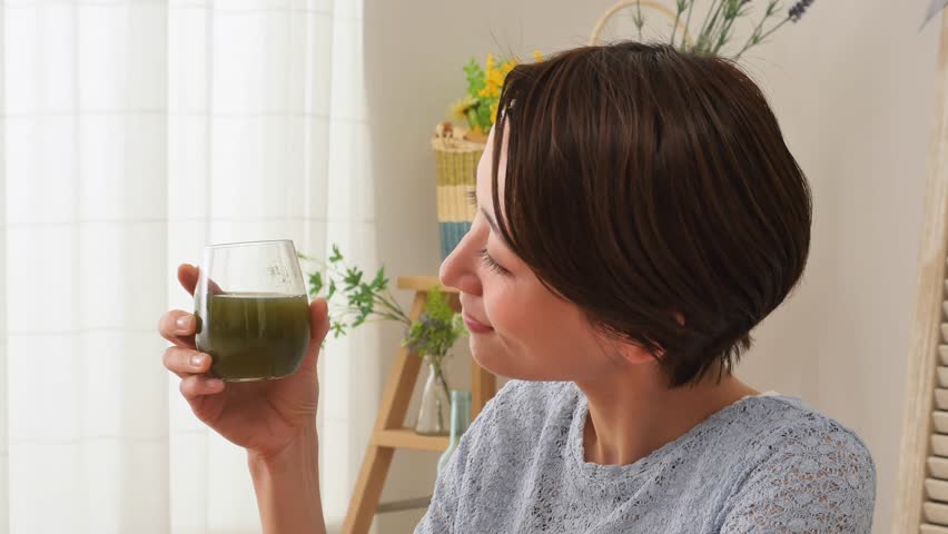 Asian woman drinking green juice at home