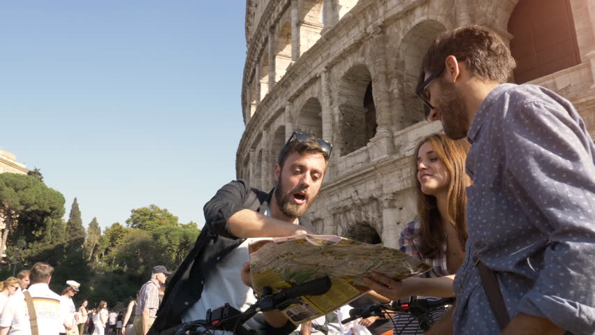Three happy young friends tourists with bikes and backpacks at Colosseum in Rome reading map guide for directions on sunny day slow motion steadycam ground shot Royalty-Free Stock Footage #1101904987