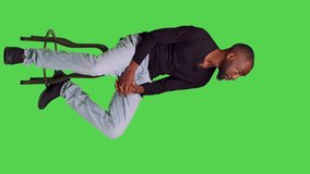 Vertical video: Side view of african american man on chair posing with confidence, sitting over full body green screen backdrop. Young male model feeling optimistic and waiting for something in studio - Powered by Shutterstock - Get 15% off with code: PIKWIZARD15