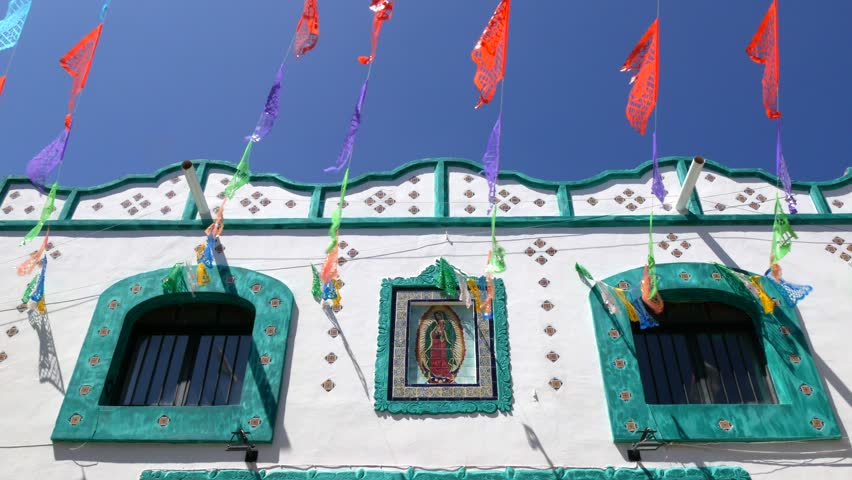 Mexican building with an image of the Virgin of Guadalupe. Colorful mexican perforated papel picado banner, festival colourful paper garland.