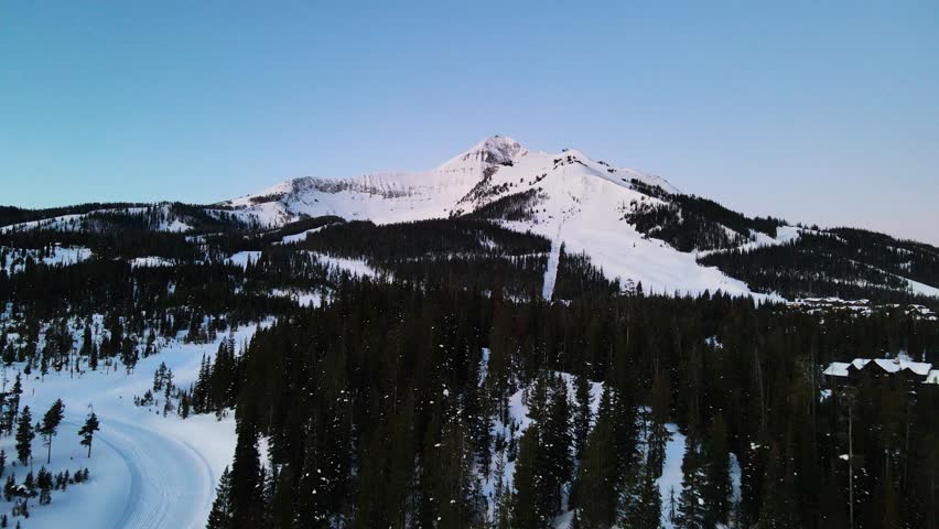 A drone shot of snowy Big Sky, Montana in winter, showcasing the ski resort and majestic mountain terrain.