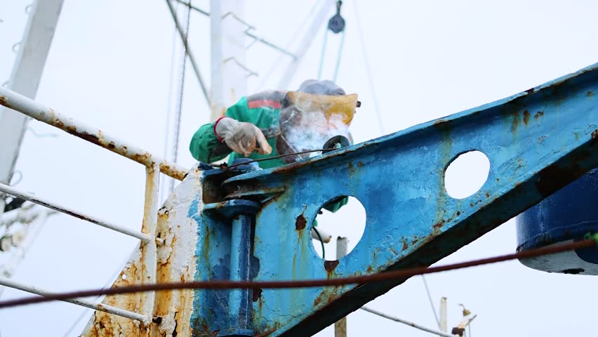 Skilled worker wears protective clothing welding and repairing metal beam