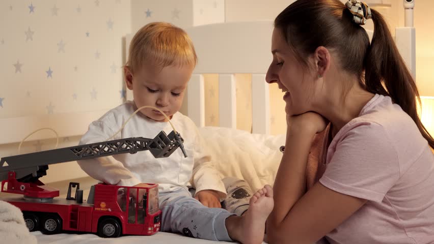 Young mother and baby boy playing with car in bed before going to sleep. Family having time together, parenting, happy childhood and entertainment