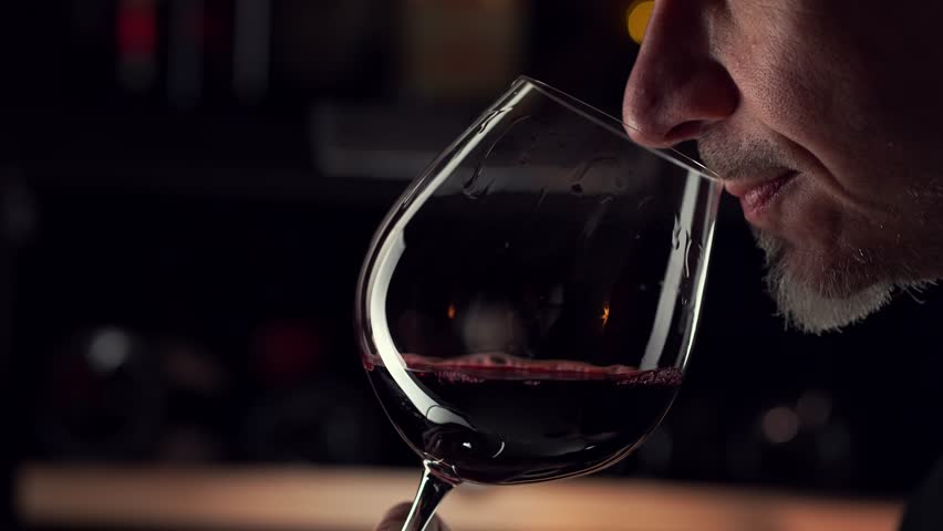 Close up man smelling red wine in wine glass. Wine expert tasting, rating and drinking wine, bottles in background. Royalty-Free Stock Footage #1101915693