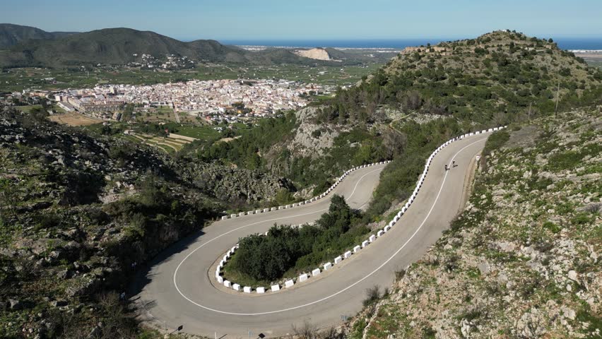 Aerial drone footage.Cyclist group in cycling kit and helmets conquering the Vall de Ebo pass in Spain.Cycling journey to the top.Сyclists ride on a winding road in the mountains.Pego,Alicante,Spain.