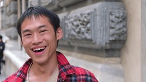 portrait of young handsome Asian man in red shirt smiling to camera in the street student blogger tourist happy emotions