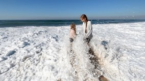Two little sisters are playing with the waves on the beach of the Atlantic Ocean. Family time or vacation concept. 4K resolution video. High quality 4k footage