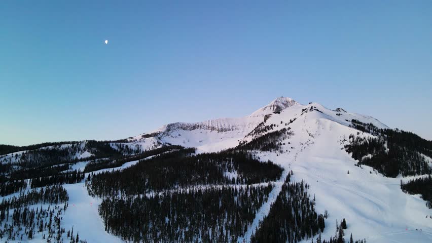 A drone shot of snowy Big Sky, Montana in winter, showcasing the ski resort and majestic mountain terrain.