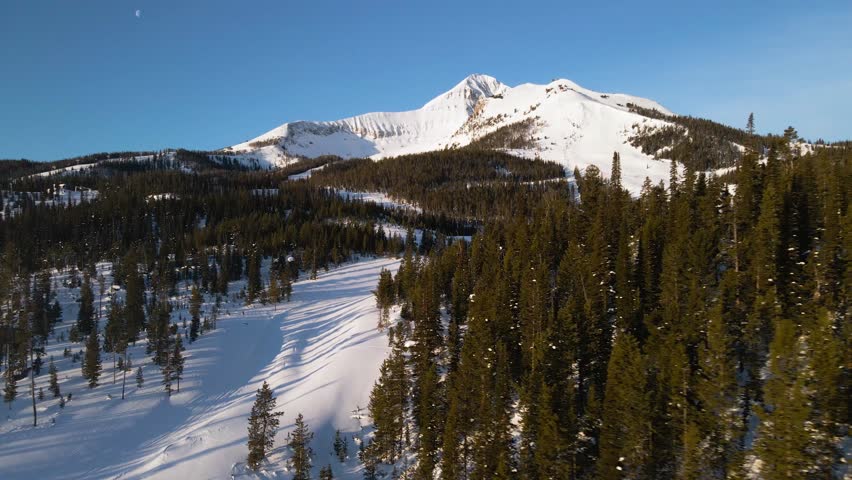 A drone shot of snowy Big Sky, Montana in winter, showcasing the ski resort and majestic mountain terrain.
