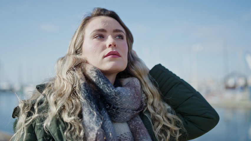 Young blonde woman standing with serious expression at seaside