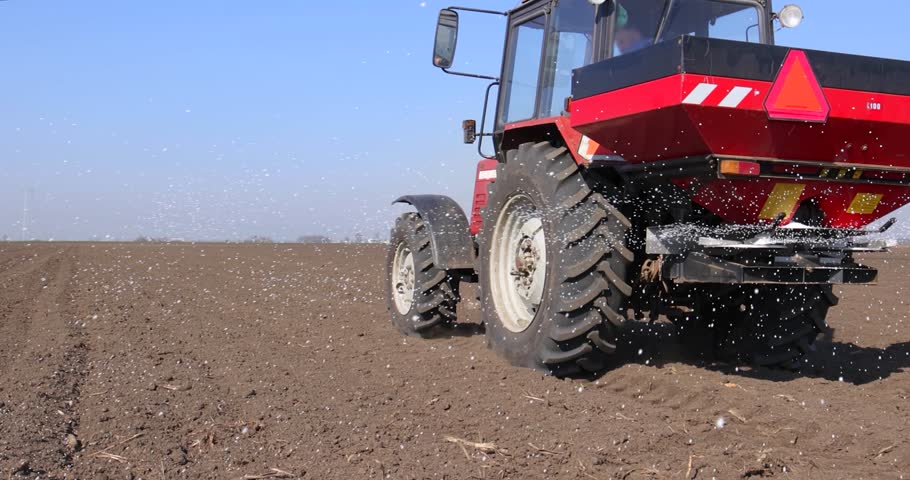 Farmer with agricultural machinery fertilizing agricultural field in spring time. Spreading mineral fertilizer, cinematic low angle gimbal shot Royalty-Free Stock Footage #1101931937