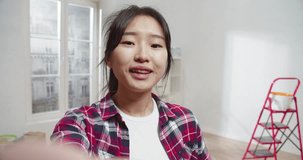 POV young cute asian woman talking on smartphone making video call showing bright flat. Renovation of apartment with equipment. Attractive beautiful female smiling and speaking.